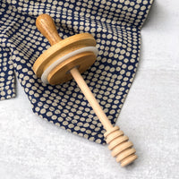 wooden honey dipper lid with wooden handle made from bamboo and beechwood on a dotted towel