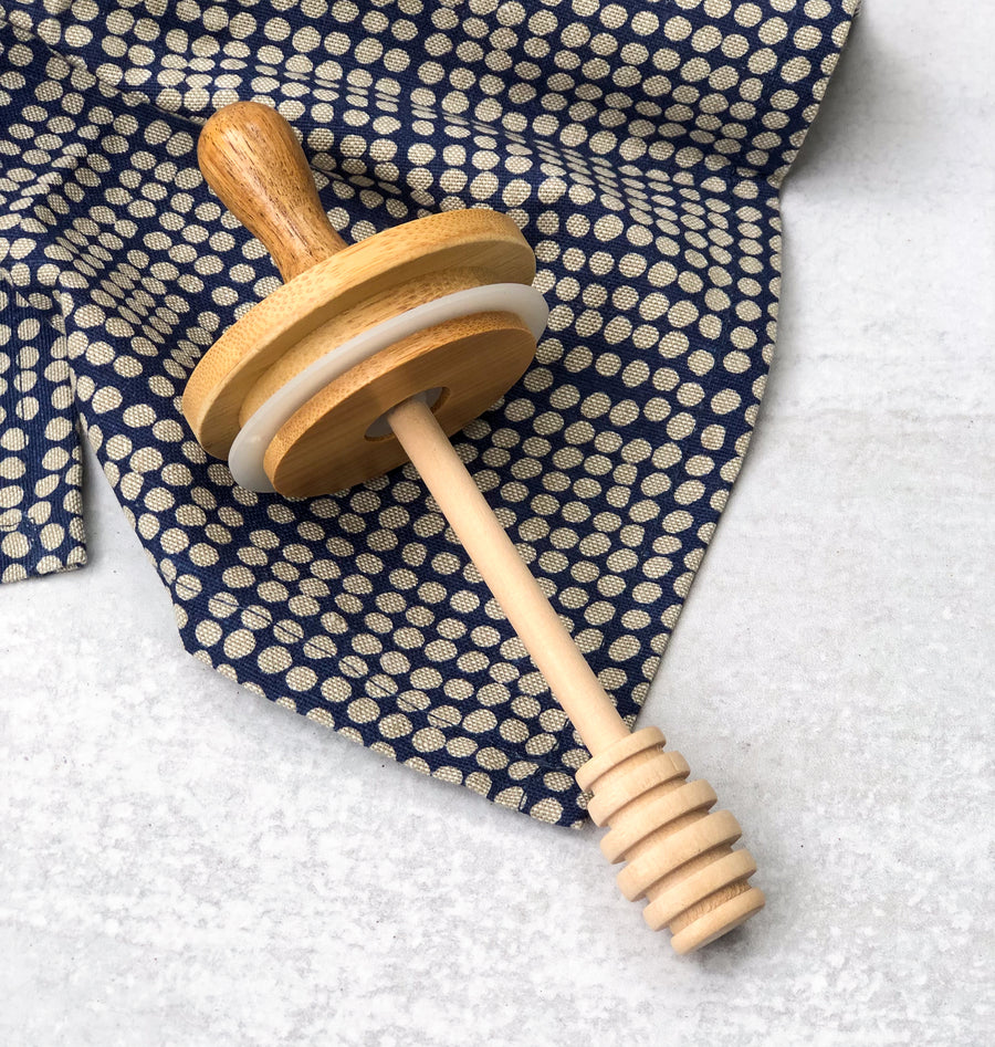 wooden honey dipper lid with wooden handle made from bamboo and beechwood on a dotted towel