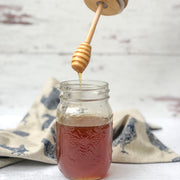 wooden honey dipper lid streaming honey into a regular mouth mason jar with chicken towel in the background